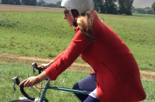 Katja mit weißem Radhelm und rotem Mantel im Sattel auf einer Radtour
