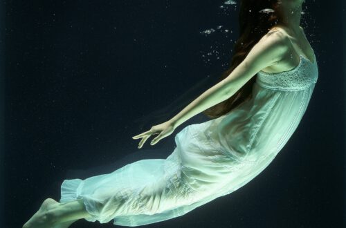 Eine Frau in einem weißen Kleid unter Wasser mit Luftblasen um Mund und Nase