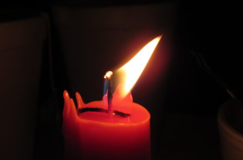 eine rote Kerze, deren Flamme sich im Lufthauch bewegt